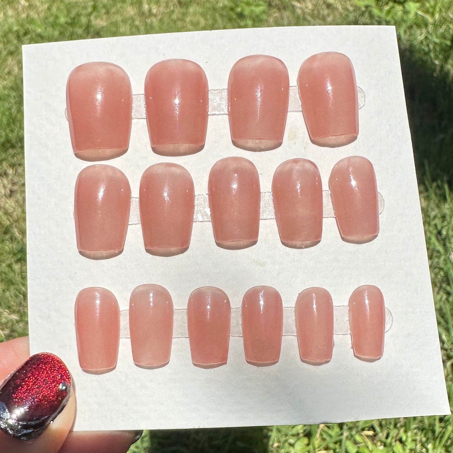 Sheet of pink nail stickers held over a grassy background