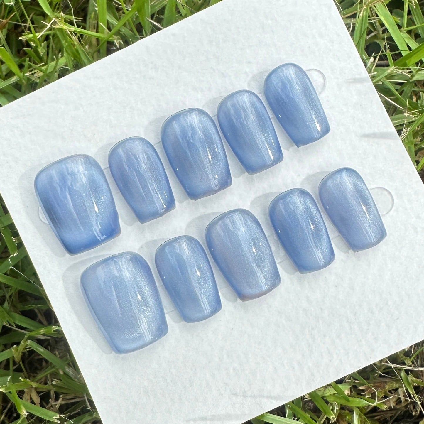 Set of blue press on nails with full moon pattern on a white card on grass
