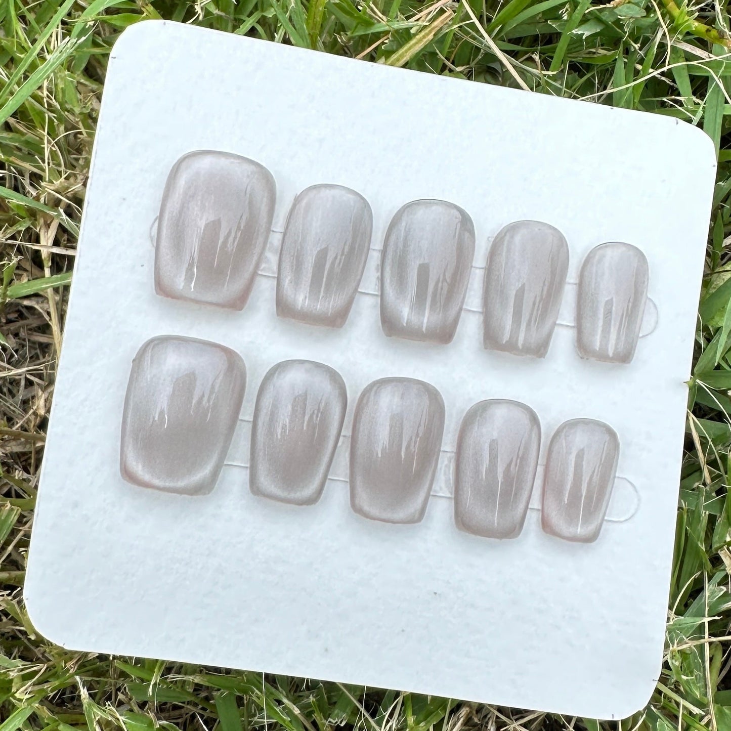 Set of press on nails in gray cat eyes a white card on grass
