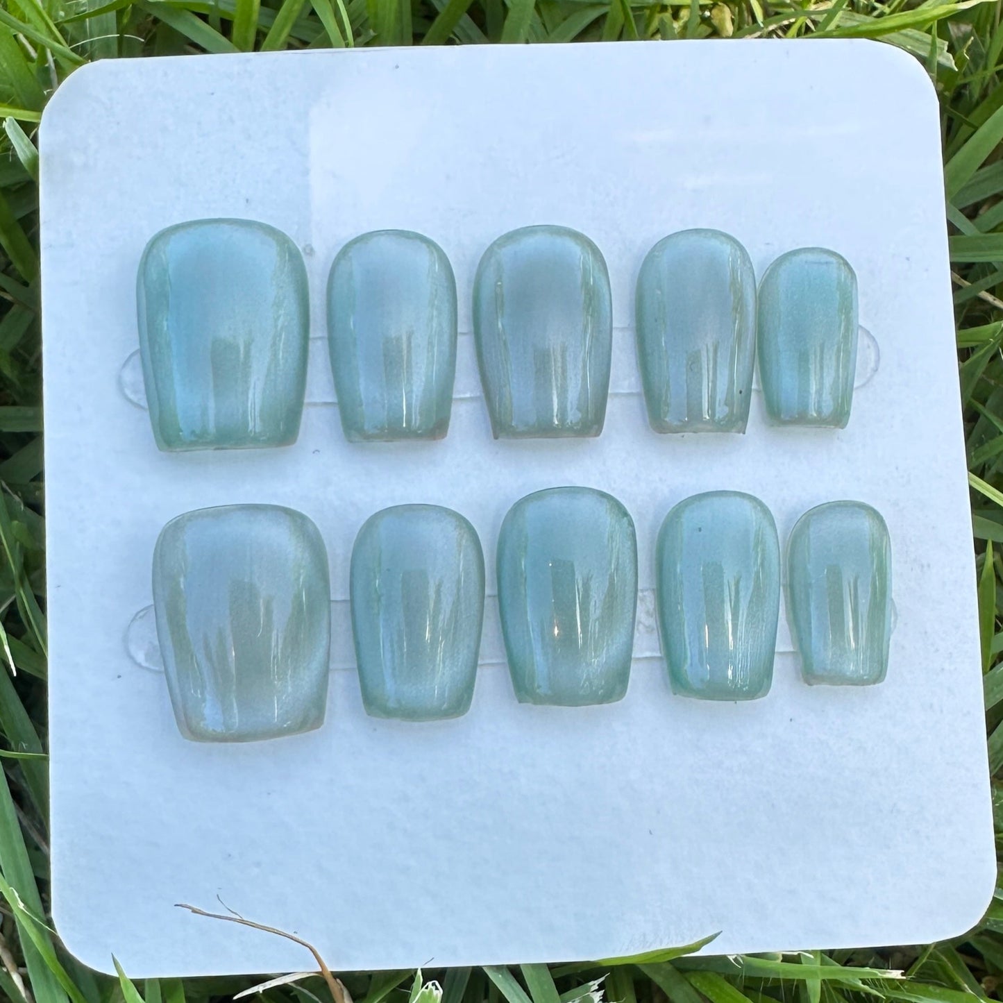 Set of light blue full moon cat eyes press on nail on a white tray with grass in the background