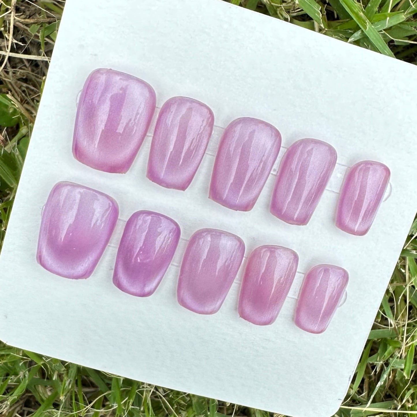 Set of purple cay eyes under the shade artificial nails on a white card lying on grass