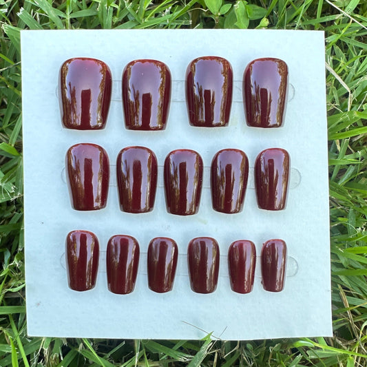 Set of brown nail polish samples on a white card with grass in the background. Handmade luxury red press-on nails flatlay