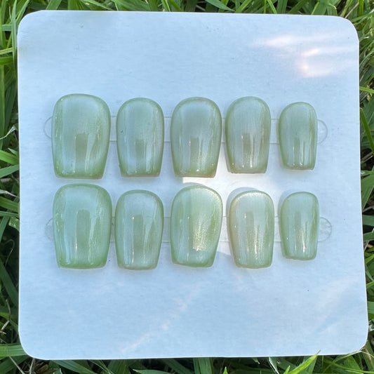Set of green nail caps on a white card with grass in the background. green cat eyes full moon  shape.