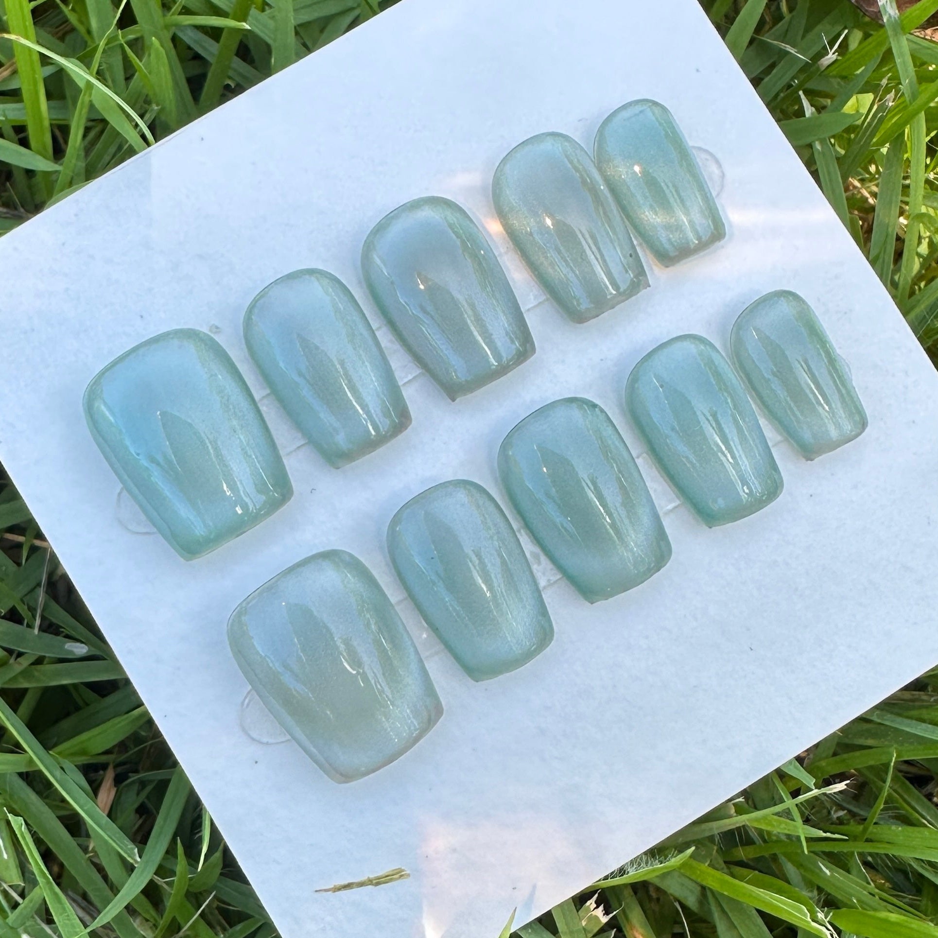 Set of light green handmade press on nail false nails on a white tray on grass. 