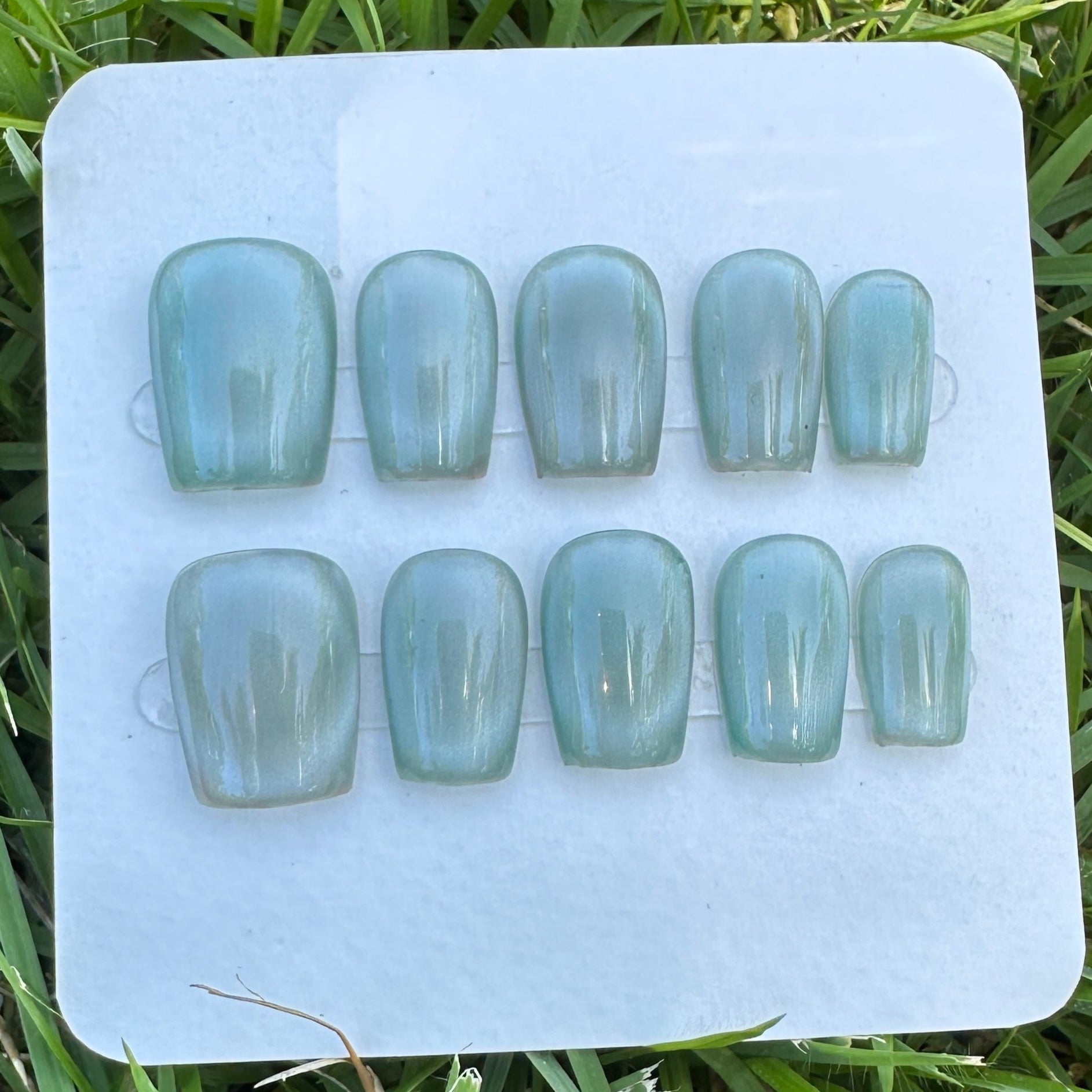 Set of light blue full moon  cat eyes press on nail on a white tray with grass in the background