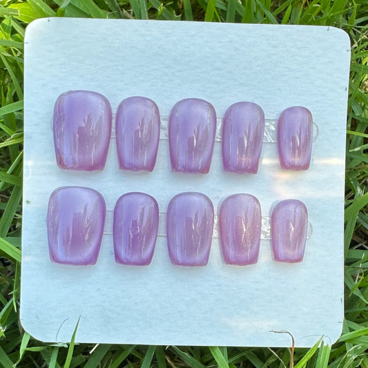Set of purple nail extensions on a clear plastic tray placed on grass. purple full moon cat eyes. 