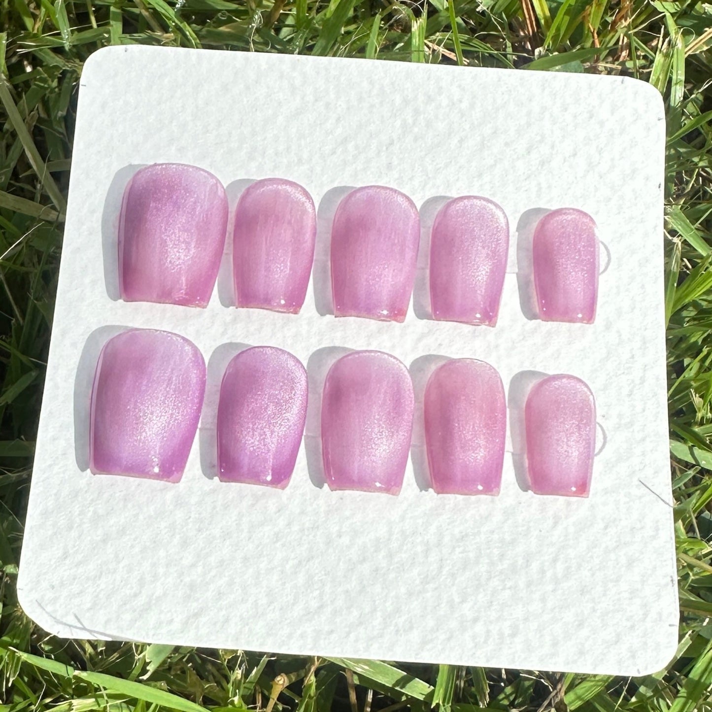 Set of purple cat eyes nail full moon shapes samples on a white card with grass in the background 