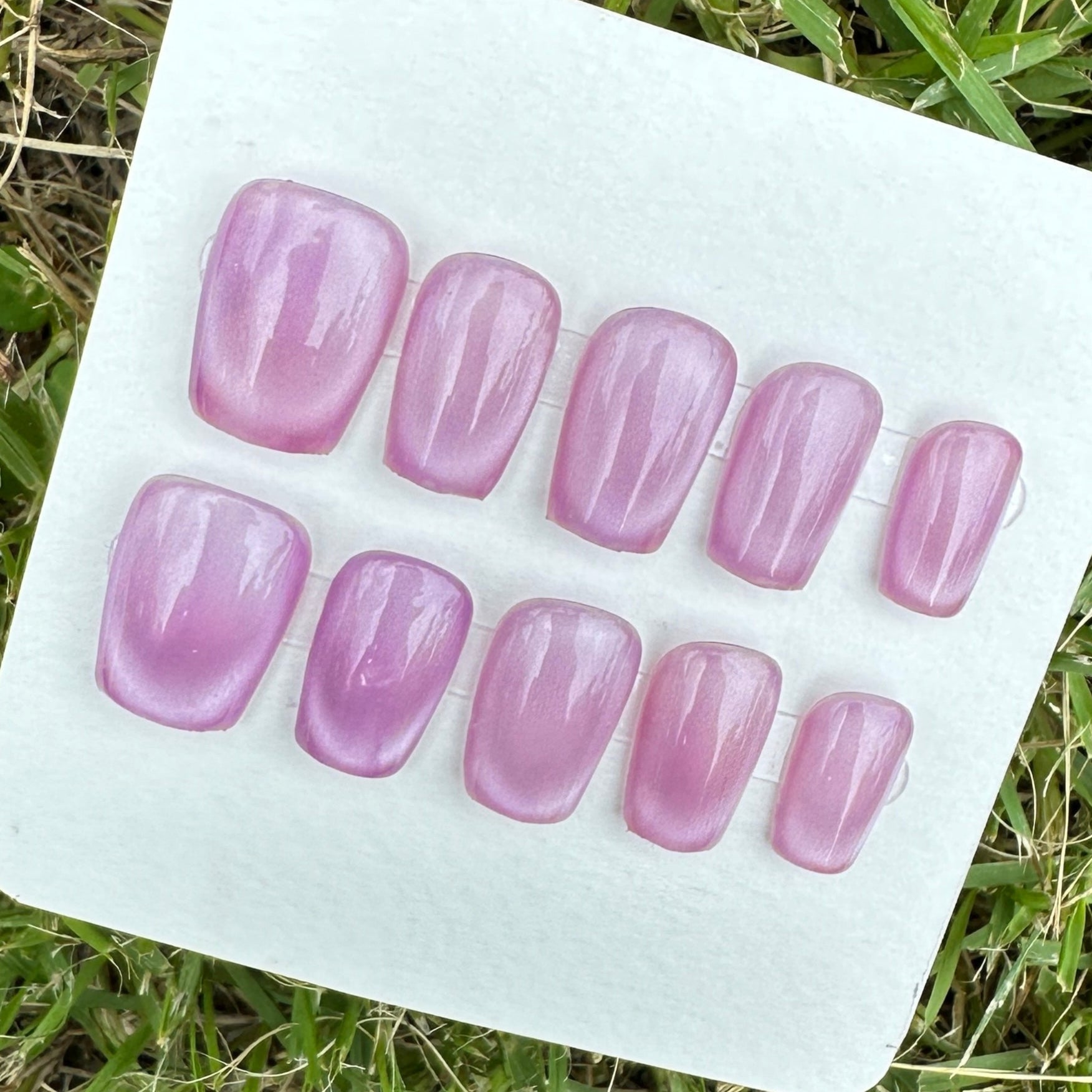 Set of purple cay eyes under the shade artificial nails on a white card lying on grass