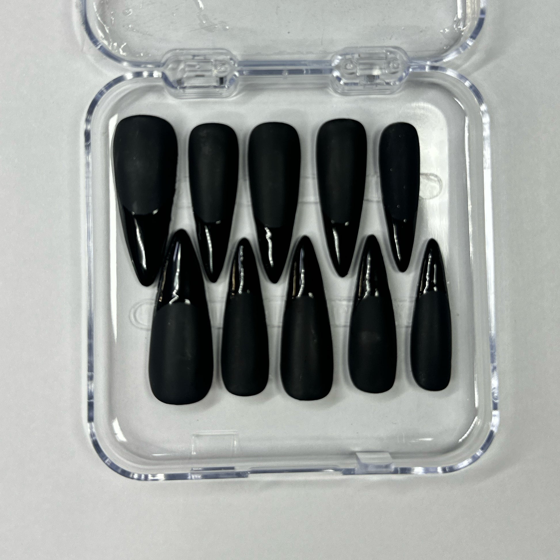 Set of black nail tips in a clear plastic case on a light gray background